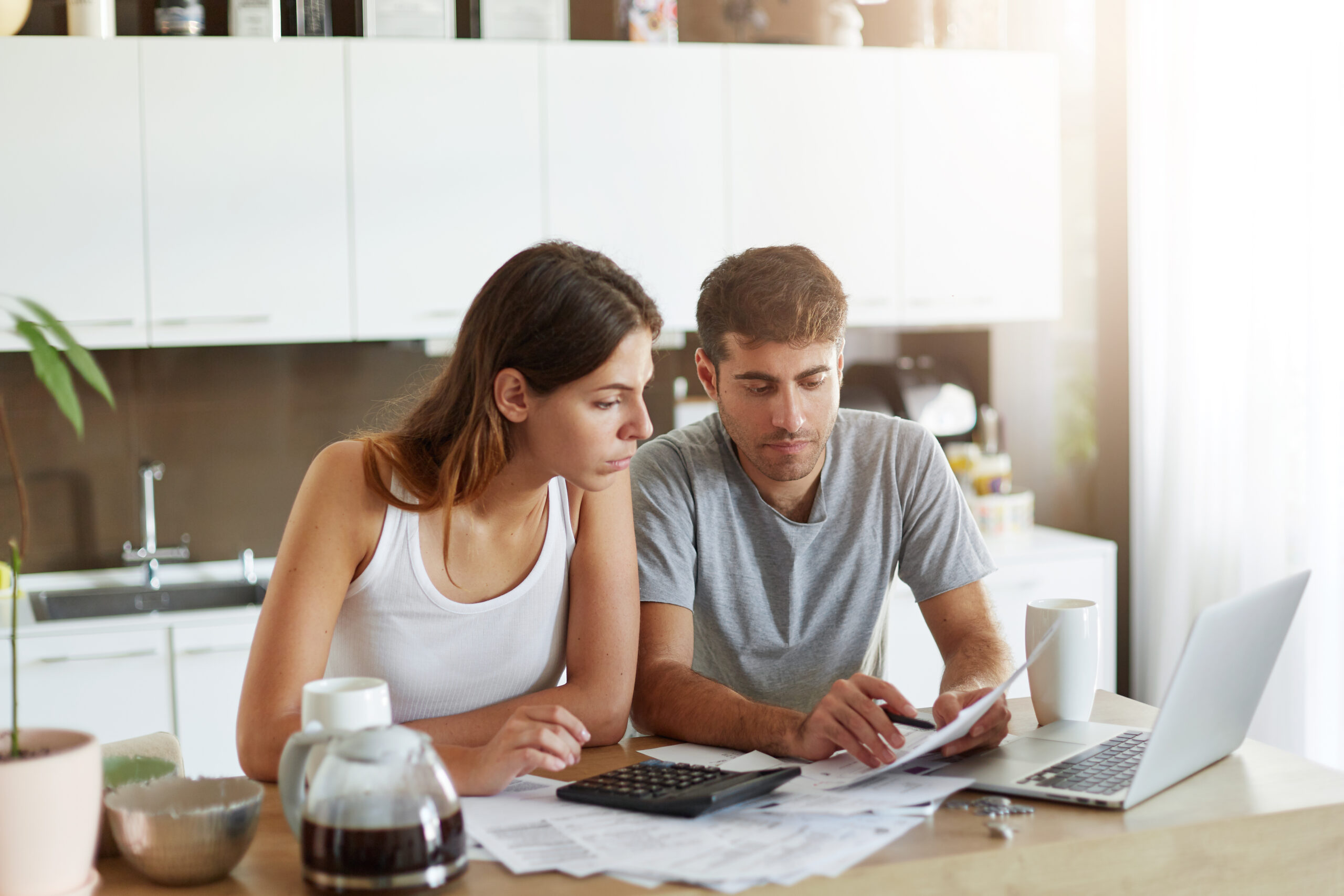 Portrait of serious man and female sitting at kitchen table, dealing with financial issues, holding documents. Family couple calculating their debts while sitting together at kitchen. Business concept